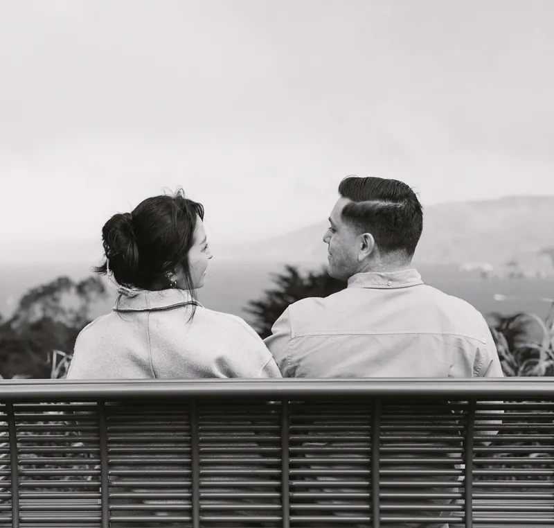 Black-and-white photo of Eden and Luis sitting on a bench, looking out over the hills