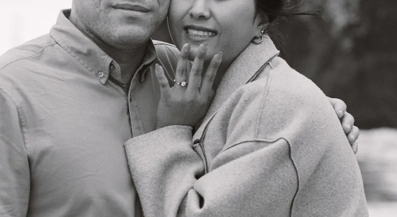 Black-and-white close-up of Eden showing the engagement ring while hugging Luis