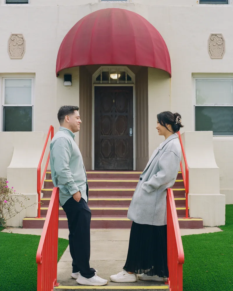 Eden and Luis facing each other on the steps beneath a red awning