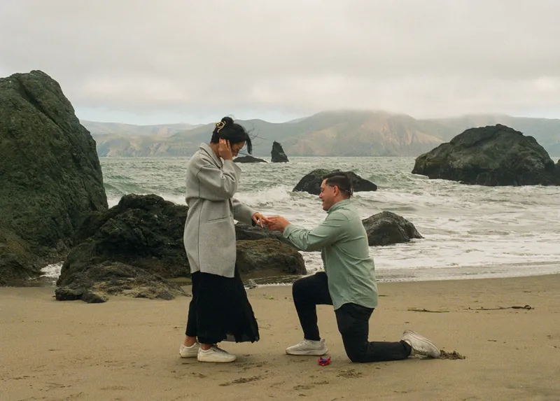 Luis kneeling and holding Eden’s hands on the beach