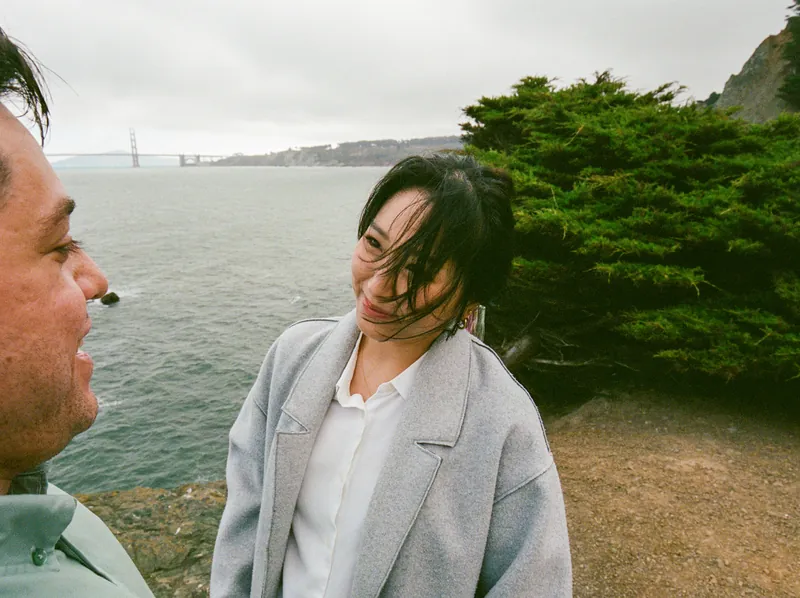 Eden smiling at Luis in front of cypress trees and the bay