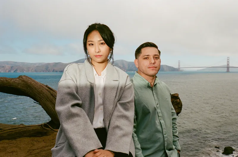 Eden and Luis sitting on a driftwood log with the Golden Gate Bridge behind them