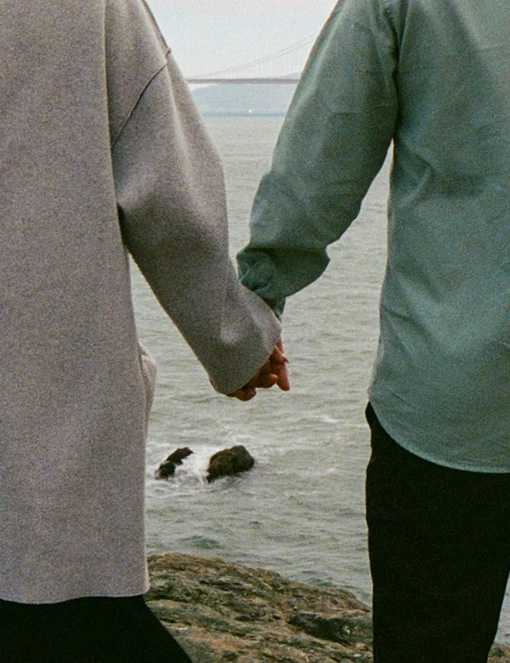 Close-up of Eden and Luis holding hands by the water