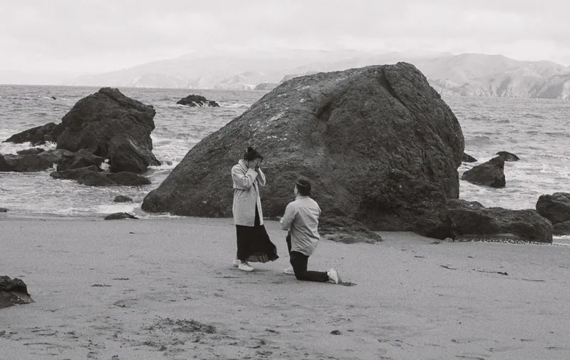 A wide view of the proposal on the beach, with the rock and the bay behind