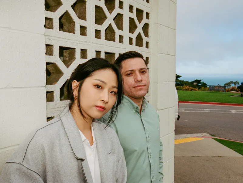 Eden leaning against Luis beside a patterned concrete wall
